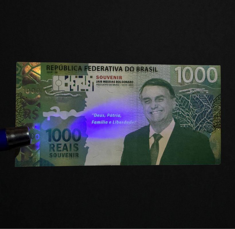 Cédula Colecionável Bolsonaro sob luz negra, com a frase Deus, Pátria, Família e Liberdade surgindo em azul